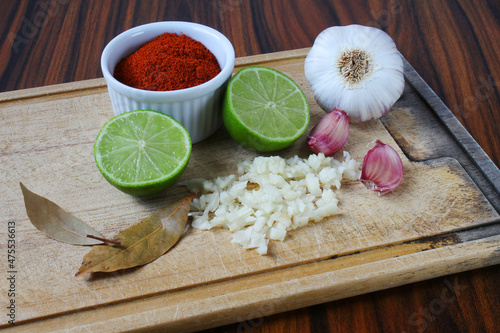 Fototapeta Naklejka Na Ścianę i Meble -  Brazilian spices. Spices in a cutting board, lemon, sliced garlic and garlic bulb, bay leaves and paprika powder.