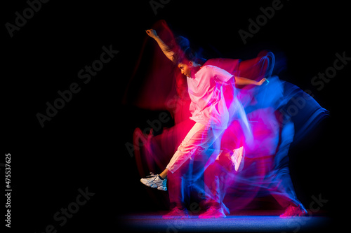 Excited young girl in white costume dancing hip-hop dance isolated on dark background at dance hall in neon mixed light.