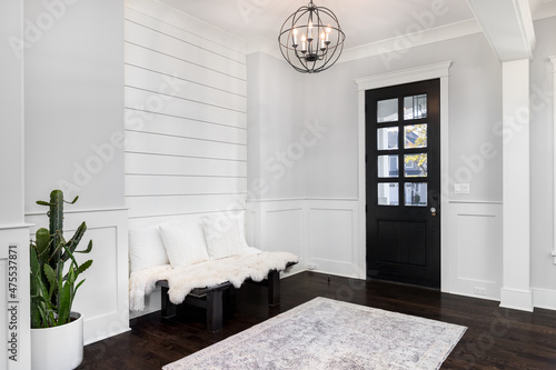 A beautiful foyer entrance with a light hanging above the dark hardwood floors, a bench in front of a shiplap wall, and a dark door with windows. photo