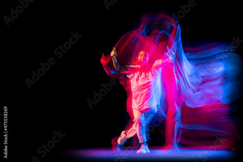 Stylish young girl in white costume dancing hip-hop dance isolated on dark background at dance hall in neon mixed light.