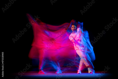 One young sportive girl in white costume dancing hip-hop dance isolated on dark background at dance hall in neon mixed light.