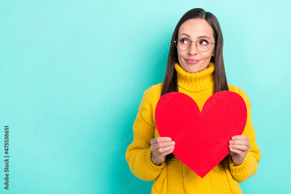 Photo of cute thoughtful woman wear yellow sweater spectacles holding large heart empty space isolated turquoise color background Photo of cute thoughtful woman wear yellow sweater spectacles holding large heart empty space isolated turquoise color background
