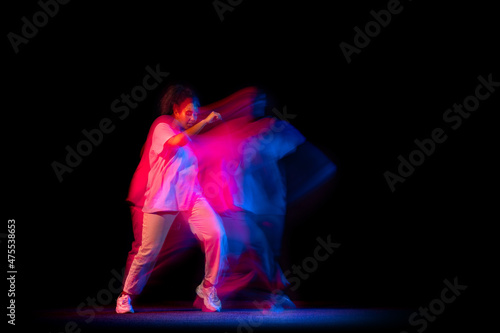 One young sportive girl in white costume dancing hip-hop dance isolated on dark background at dance hall in neon mixed light.
