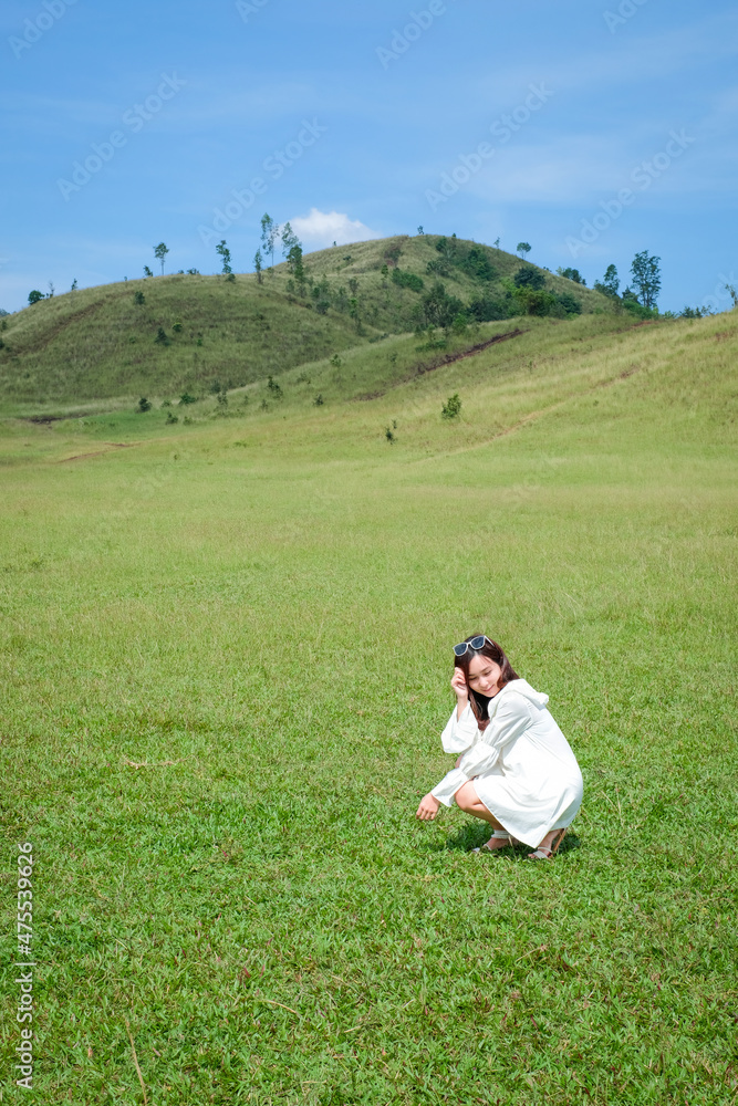 Beautiful Girl stand and acting in front of bald mountain or Phu Khao Ya with green grass field and blue sky. One of natural travel attraction in Ranong province, Thailand