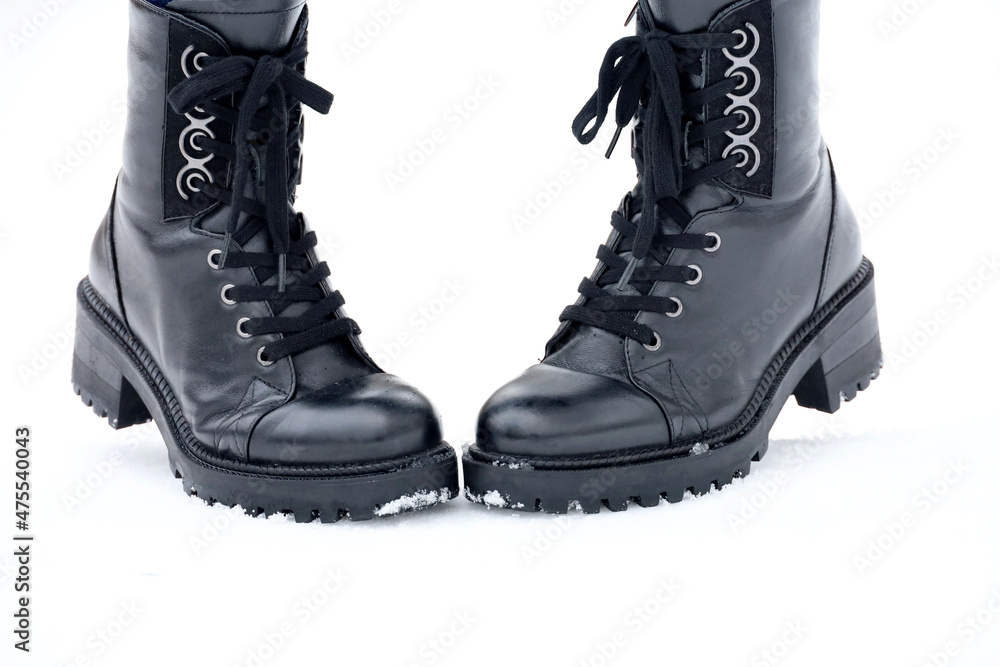 Female legs in black leather lace-up boots on a snow. Woman on winter street, warm footwear for cold weather