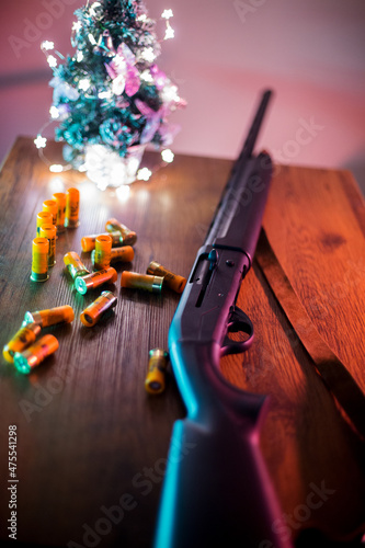 shotgun and cartridges on the wooden table near a christmas tree in cyan and neon light