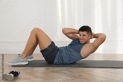 Handsome man doing abs exercise on yoga mat indoors