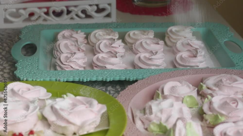 A woman sprinkles powdered sugar on marshmallows and marshmallow roses. Close-up shot. A woman sprinkles powdered sugar on marshmallows and marshmallow roses. Close-up shot.