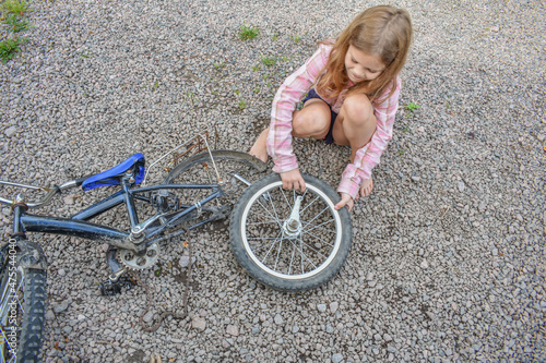 the child girl has damaged a bicycle wheel and is making repairs photo without processing