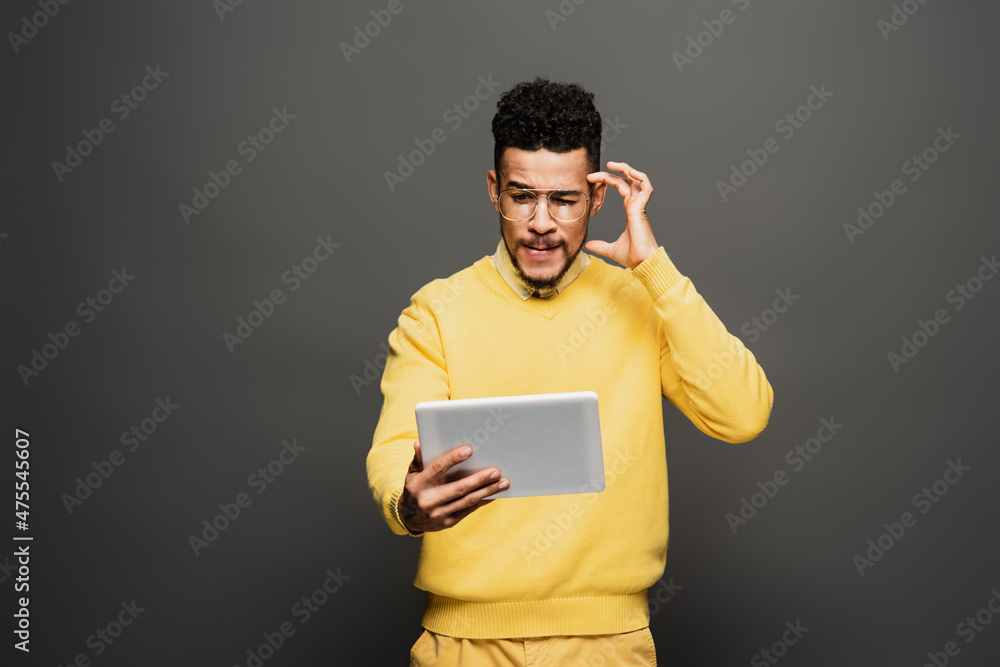 thoughtful african american man in glasses using digital tablet on dark grey. thoughtful african american man in glasses using digital tablet on dark grey.