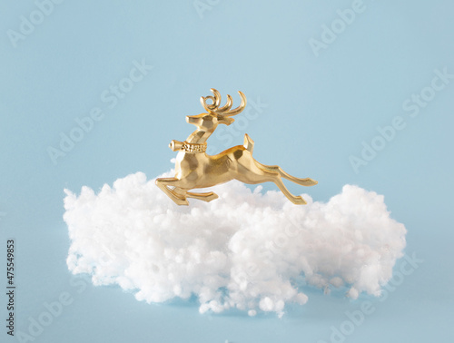 Golden reindeer Christmas decoration on fluffy cloud against pastel blue background. Happy New Year idea, winter holidays. 
