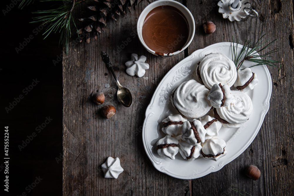 Meringue cookies with chocolate and almond cream and cup of hot chocolate, wrapped presents and natural winter decorations on old wooden table 
