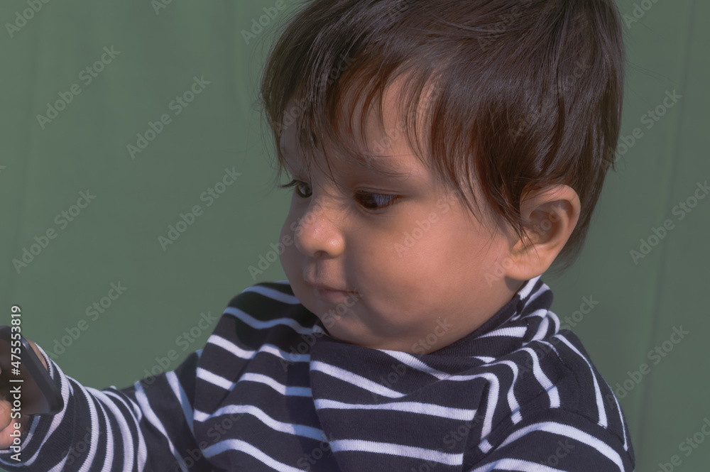 Baby looking at mobile phone. Sweet small baby with mobile phone on a isolated background. Head shot portrait. Front View. Close up. Indian ethnicity. Baby looking at mobile phone. Sweet small baby with mobile phone on a isolated background. Head shot portrait. Front View. Close up. Indian ethnicity.