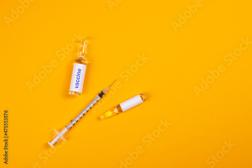 The concept of protection against the COVID-19 virus. Syringe and ampoule with a vaccine on a yellow background.
