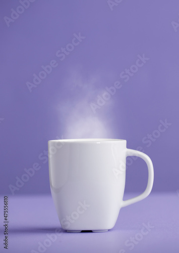White ceramic cup of coffee or tea with hot steam, with a purple background (very peri).