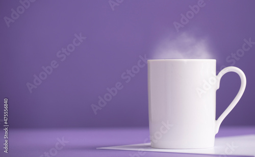 White ceramic cup of coffee or tea with hot steam, with a purple background (very peri).