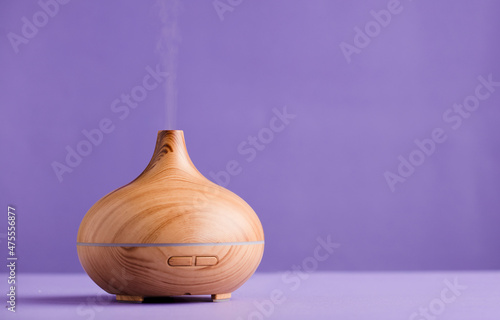 Foto Essential oil air freshener in wood with steam, with a violet background (very peri)