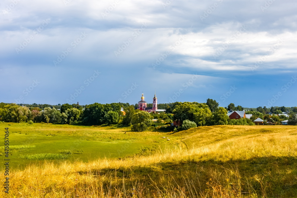 Obraz premium Summer landscape with buildings, churches, trees, shrubs, grass, sky with clouds of the city of Suzdal in Russia