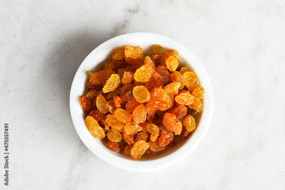 A top view image of yellow seedless raisins in a white ceramic bowl. A top view image of yellow seedless raisins in a white ceramic bowl.