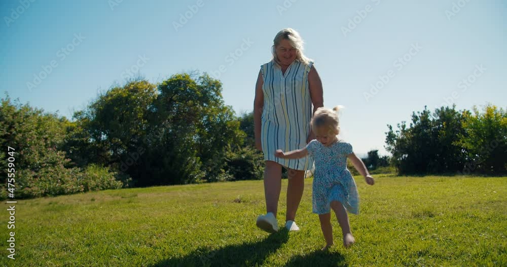 Happy family dancing on public park at sunny summer day. Middle aged woman doing exercises with her granddaughter on green grass. Concept of carefree time together grandmother with cute baby girl. Happy family dancing on public park at sunny summer day. Middle aged woman doing exercises with her granddaughter on green grass. Concept of carefree time together grandmother with cute baby girl.
