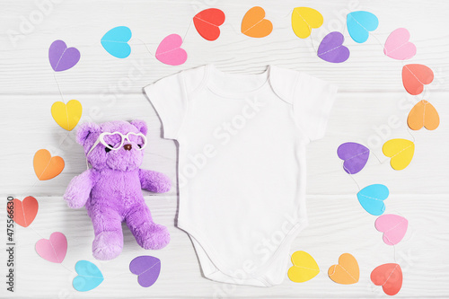 Mockup white baby shirt with paper colorful hearts. Happy Valentines Day baby apparel flatlay on white wood background  flat lay  top view  copy space.