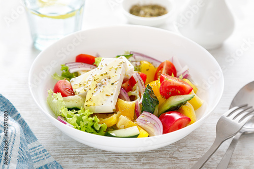 Fresh summer vegetable salad with lettuce, tomato, cucumber, bell pepper, onion and feta cheese, dressed with olive oil
