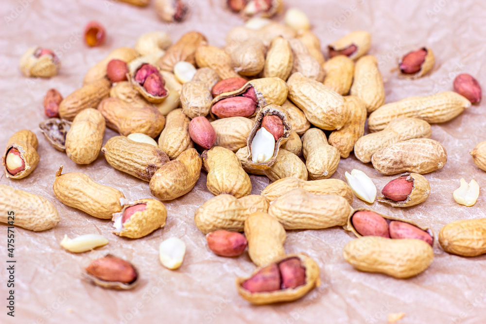 Raw unpeeled peanut nuts in nutshell heap on light paper background.