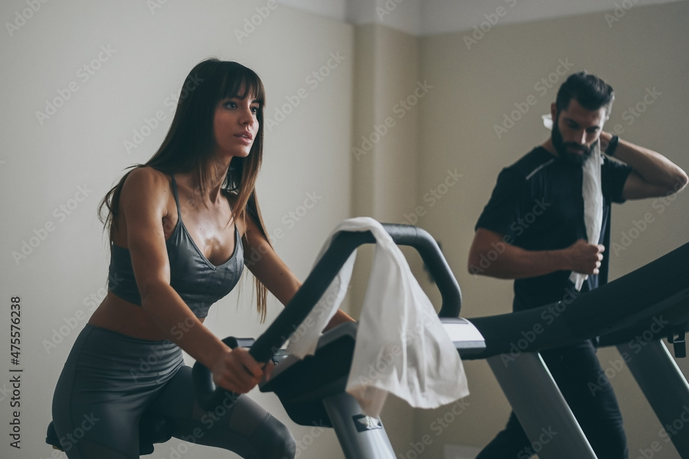 Determined young couple working out in gym. Fit boy and girl doing exercise  with cyclette and tapis roulant. Beautiful sporty woman. Strong boys works  out together. Wellness, health, sport, concept. Stock Photo