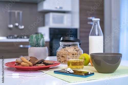 Table set for breakfast  kitchen in the background. Natural meal cup of milk  cereal cookies and fruits. Interior view of a cozy and modern home in the morning Happiness  youth health positive concept