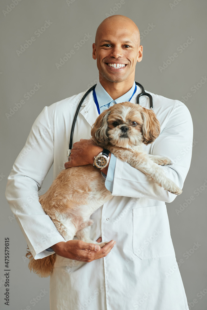 Happy African American veterinarian with dog looks at camera.