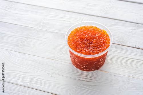 red caviar in a plastic jar on a white wooden background