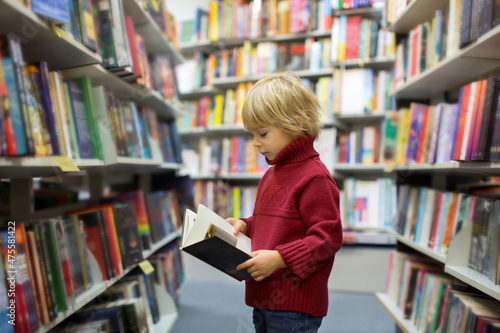 Cute blond toddler child, boy, reading book in a book store
