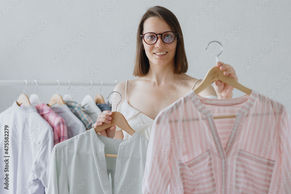 a European woman professional stylist with dark hair and glasses chooses clothes for a business meeting or dinner. millennial housewife woman disassembles home wardrobe for washing or recycling. a a European woman professional stylist with dark hair and glasses chooses clothes for a business meeting or dinner. millennial housewife woman disassembles home wardrobe for washing or recycling. a