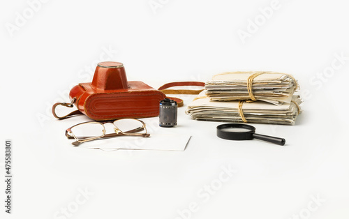A stack of family photos and a film camera, glasses and a magnifier on a white background.