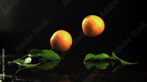 Fresh tangerines fall on the table. On a black background.Filmed is slow motion 1000 frames per second. High quality FullHD footage photo