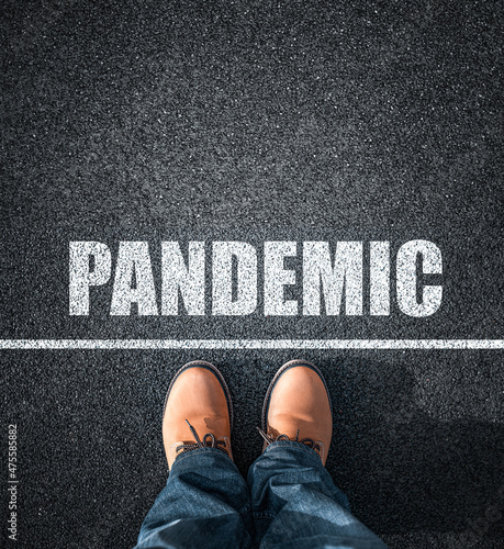 Obraz na płótnie Inscription Pandemic on the asphalt. Feet in boots against the background of the inscription about Pandemic. w salonie