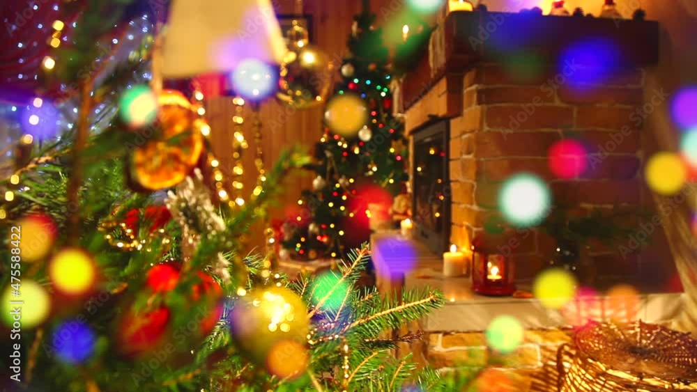 New Years interior of a wooden house with a fireplace, a Christmas tree with twinkling garlands, gifts and candles. Shifting the focus to the fir branches and balls in the foreground. New Years interior of a wooden house with a fireplace, a Christmas tree with twinkling garlands, gifts and candles. Shifting the focus to the fir branches and balls in the foreground.