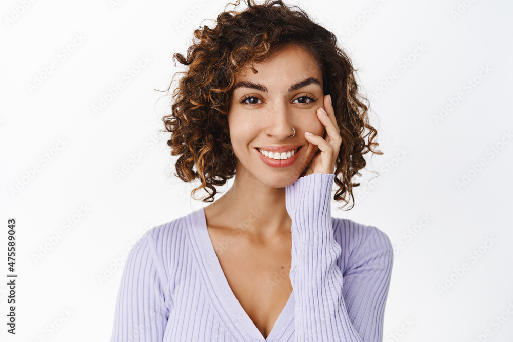 Close up portrait of beautiful curly woman, middle-eastern girl with glowing healthy skin, touching face and smiling happy, standing over white background Close up portrait of beautiful curly woman, middle-eastern girl with glowing healthy skin, touching face and smiling happy, standing over white background