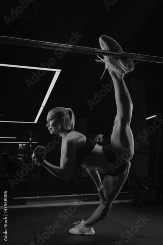 A woman with blonde hair is doing a twine during dumbbell bicep curls in a gym.