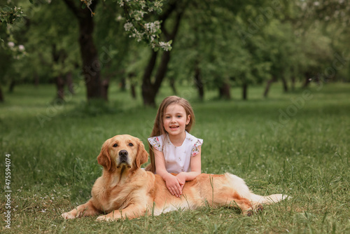 a girl in a white dress and a straw hat in a blooming garden hugs a dog Golden Retriever Labrador