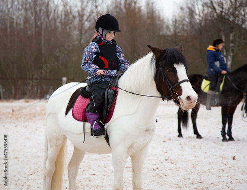 Girl rides on a white horse. Hippotherapy for young children is the prevention of spinal diseases, as well as therapy after many serious diseases © sergeialyoshin