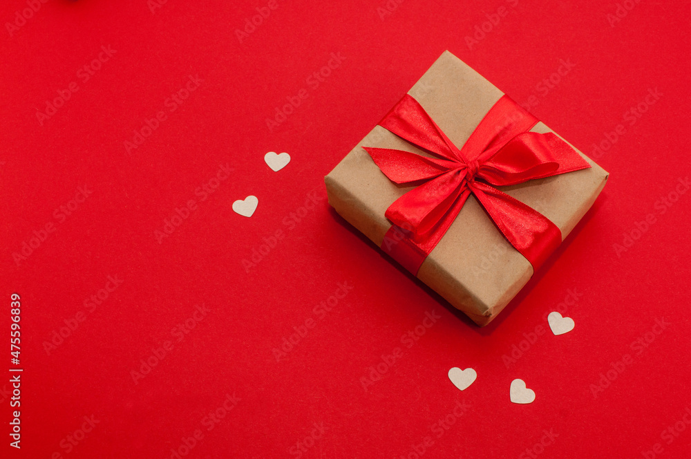 gift box in craft packaging and with a red ribbon on a red background with hearts gift box in craft packaging and with a red ribbon on a red background with hearts