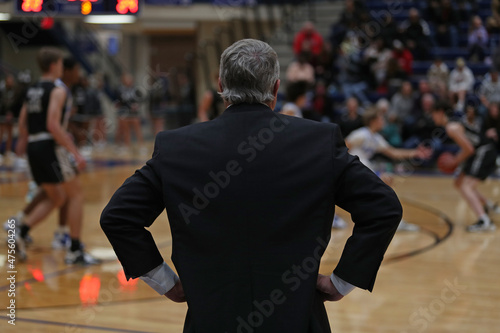 A high school basketball coach, with hands on hips, watches the action.
