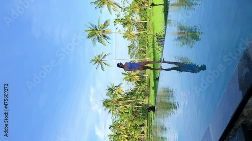 Beautiful women relaxing and walking on the edge of infinity pool overlooking rice terraces and palms on Bali island .Palms trees are reflected in the water. High vertical quality 4k footage photo
