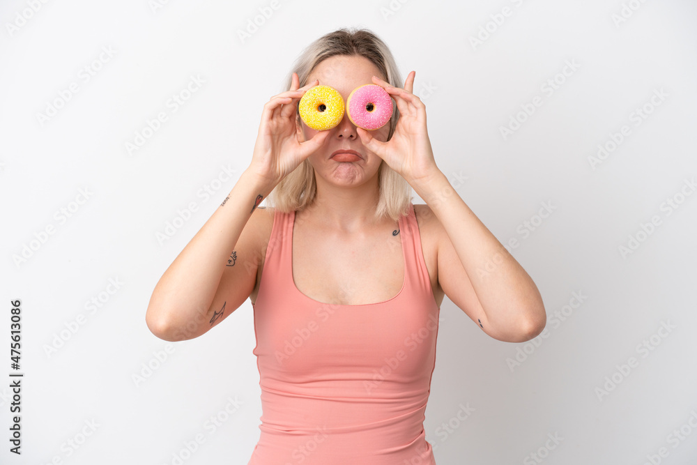 Young caucasian woman isolated on white background holding donuts in eyes with sad expression Young caucasian woman isolated on white background holding donuts in eyes with sad expression