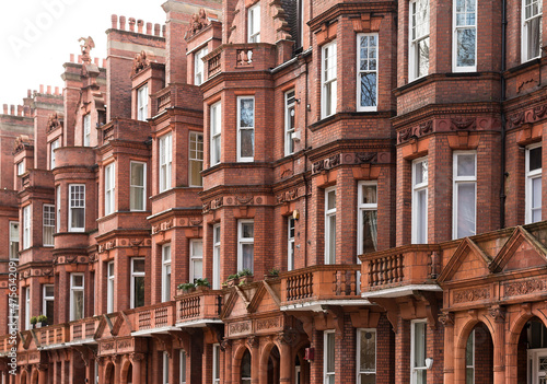 A row of English terraced homes featuring typical British architecture with prominent red terracotta brickwork, tall chimneys and intricate detailing.
