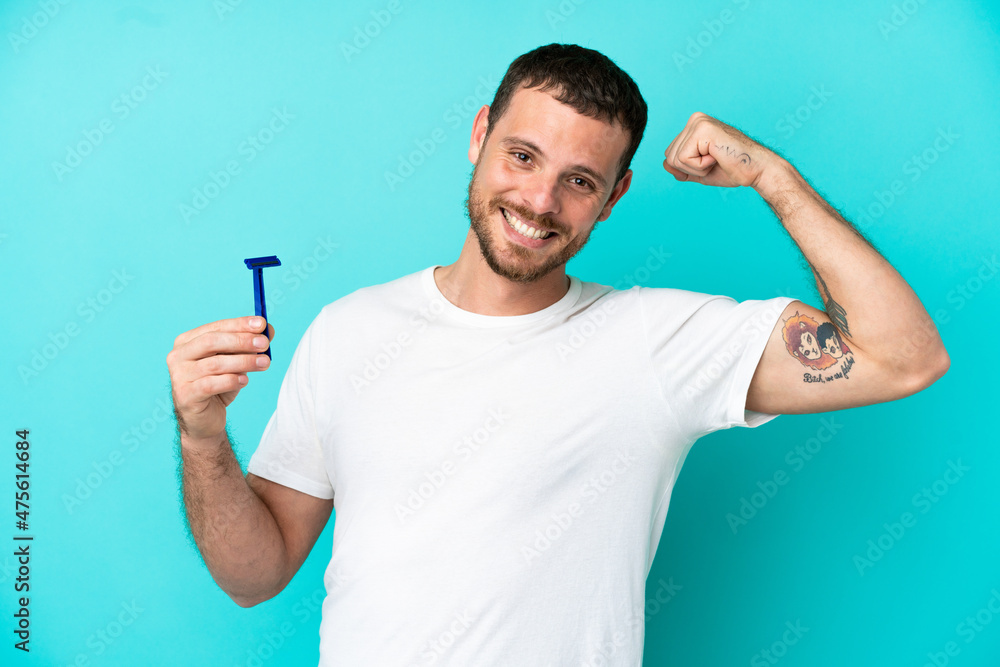 Brazilian man shaving his beard isolated on blue background doing strong gesture Brazilian man shaving his beard isolated on blue background doing strong gesture