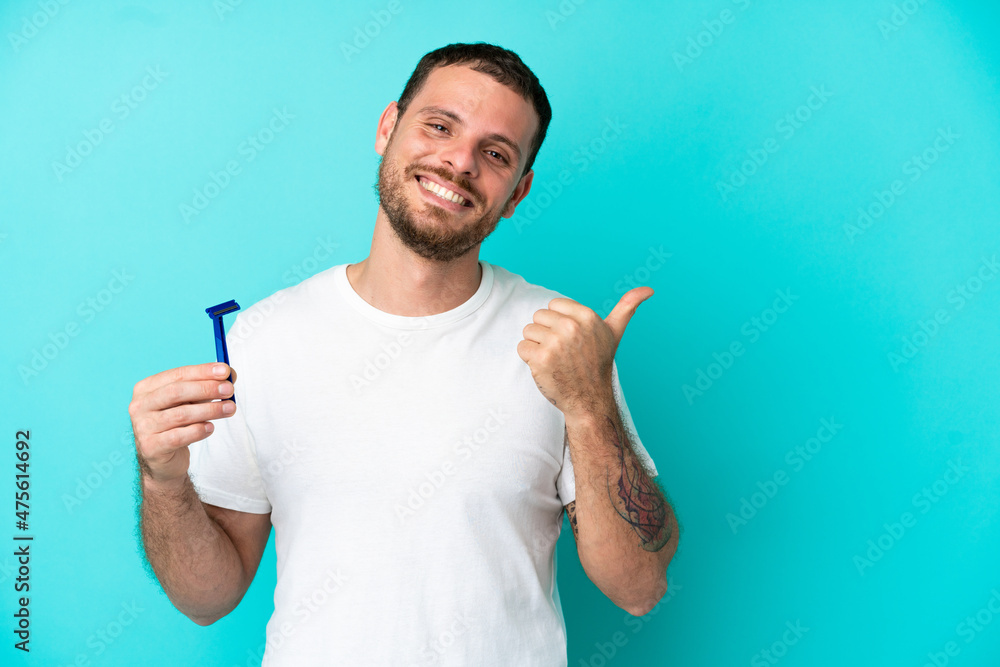Brazilian man shaving his beard isolated on blue background pointing to the side to present a product Brazilian man shaving his beard isolated on blue background pointing to the side to present a product
