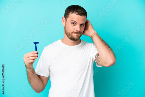 Brazilian man shaving his beard isolated on blue background having doubts