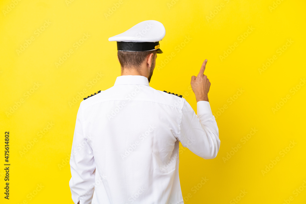 Airplane caucasian pilot isolated on yellow background pointing back with the index finger